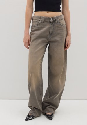 Weit geschnittene, ausgewaschene graue Jeans mit Fronttaschen und Gürtelschlaufen, kombiniert mit schwarzen spitzen Absätzen mit weißen Polka-Dots. Strukturierter Denimstoff.