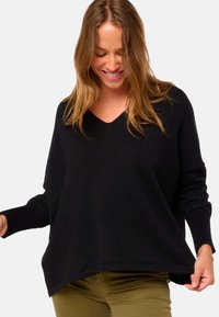 Schwarzer V-Ausschnitt-Pullover aus weichem Strickmaterial, mit lockerer Passform und langen Ärmeln, einem leicht abgerundeten Saum und gerippten Details.