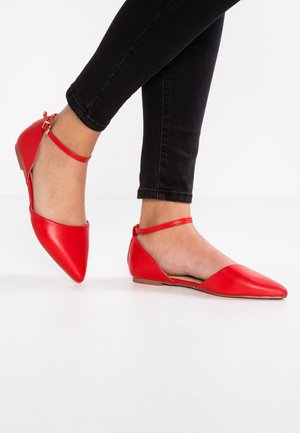 Zapatos planos de cuero rojo con punta afilada y correa en el tobillo. Textura suave, diseño minimalista y tacón bajo.