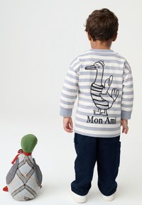 Striped gray and white long-sleeve top with duck graphic and "Mon Ami" text on the back; paired with dark blue pants and cream shoes.
