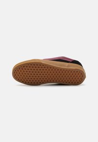 Chaussure noire et rose avec une semelle en caoutchouc, présentant un motif texturé pour une meilleure adhérence et une partie supérieure lisse. Détail de blocage de couleur distinctif.
