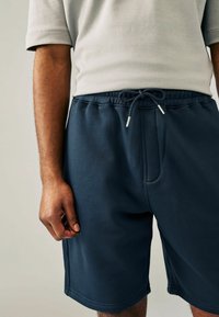 Pantalones cortos deportivos en azul marino con cinturilla elástica y cordón. Confeccionados con una tela suave y lisa, cuentan con bolsillos laterales y un ajuste a medida.