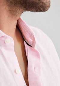Lichtroze blouse met kraag van een gestructureerde stof, voorzien van een knoopsluiting en contrasterende zwarte accenten nabij de kraag.