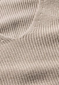Beige gestrickter Stoff mit gerippter Textur und gleichmäßig verteilten vertikalen Linien, die ein glattes und konsistentes Aussehen erzeugen.