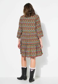 Langärmliges, gemustertes Kleid in lebhaften Farben mit einem faltigen Rock. Tragen mit schwarzen Cowboystiefeln und weißen Socken mit floralem Muster.