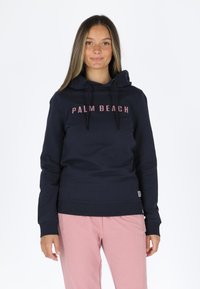 Felpa navy con testo rosa "PALM BEACH", cappuccio con lacci, polsini e orlo a costine. Abbinata a pantaloni rosa chiaro. Materiale misto cotone.