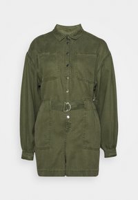 Zielono-oliwkowy dżinsowy kombinezon z zapięciem na guziki z przodu, dwoma kieszeniami na piersi, paskiem w talii z srebrnym pierścieniem oraz długimi rękawami zgromadzonymi przy mankietach.