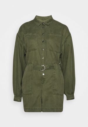 Oliivinvihreä farkkukansapuku, jossa on napitettu etuosa, kaksi rintataskua, vyötäröllä hopeinen rengas ja pitkät hihat, jotka on koottu hihoista.