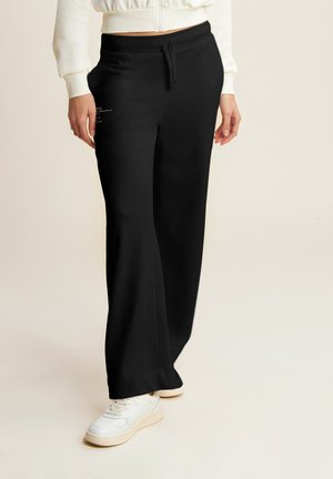 Pantalones de chándal negros con un ajuste relajado, cintura con cordón y bolsillos laterales. La tela parece suave con una textura lisa.