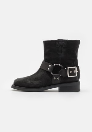 Stivali alla caviglia in suede nero con punta rotonda, cinturino laterale con fibbia e dettagli in metallo argentato. Tacco corto a blocco e finitura testurizzata.