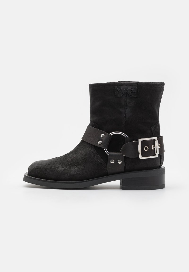 Botas de tobillo de ante negro con punta redonda, correa lateral con hebilla y acentos de hardware plateado. Tacón corto y acabado texturizado.