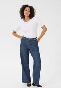 Jeans larges bleu marine avec poches avant, texture en denim et coutures contrastées ; associés à un haut ajusté à manches courtes blanc.