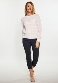 Helles rosa Sweatshirt mit horizontalen Spitzenmustern, kombiniert mit schwarzen schmal geschnittenen Hosen und nudefarbenen Schuhen. Glatte Textur und Rundhalsausschnitt.