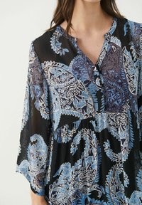 Mustapuku sinisellä paisley-kuvalla, jossa on lovikaulus, pitkät hihat ja lentävä siluetti. Valmistettu kevyestä kankaasta.