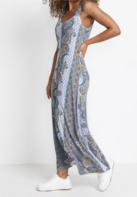 Maxi šaty z modré látky s paisley a geometrickými vzory. Bezrukávový design, lehký materiál, s bočními rozparky, v kombinaci s bílými teniskami.