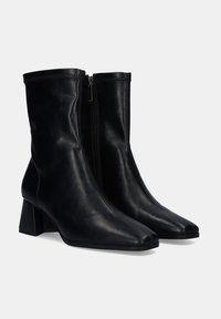 Botines de cuero negro hasta el tobillo con punta afilada y tacón cuadrado. Disponen de una cremallera lateral y textura suave. Diseño simple y elegante.