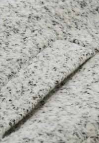 Tissu texturé gris et blanc avec une apparence duveteuse ; présente un motif de petites taches noires, créant un effet moucheté.