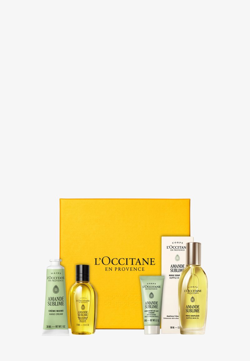 L'Occitane almond-scented skincare set with hand cream, body oil, and milk concentrate in green and amber bottles beside a yellow branded box.
