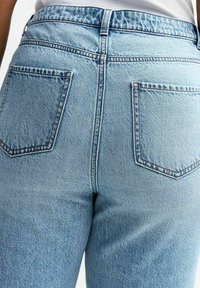 Ljusblå denimjeans med hög midja, med två bakfickor och synlig sömnad längs sömmarna och fickkantarna.