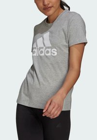 Szara koszulka z krótkim rękawem z dużym białym logo Adidas z przodu, wykonana z miękkiego, lekkiego materiału.