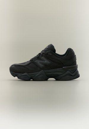 Μαύρο αθλητικό παπούτσι New Balance με πλέγμα στα πλαϊνά, παχιά υφή στην σόλα και κλείσιμο με κορδόνια, εμφανιζόμενο από πλευρά σε ουδέτερο φόντο.