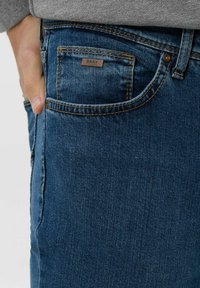 Jeans in denim blu scuro con taglio dritto, dotati di una piccola tasca frontale e di un'etichetta in pelle. Dettagli cuciti in arancione a contrasto.