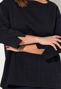 Top blu navy in tessuto testurizzato con motivo a quadrati; presenta maniche a tre quarti con ritagli angolati e scollatura a barca.