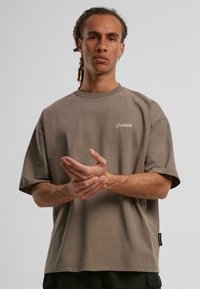 Šedé bavlněné oversized tričko s krátkým rukávem, kulatým výstřihem a malým bílým logem "Prohibováno" na hrudi; visačka na boku.