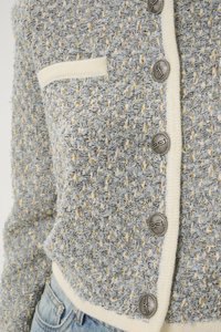 Lys blå strukturet cardigan med metalltråder, kremfargede detaljer og sølvknapper. Inkluderer en lomme på venstre side.