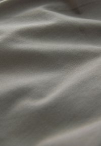 Tissu gris doux et lisse avec une texture subtile de tissage diagonal et des plis délicats créant des variations de lumière et d'ombre.
