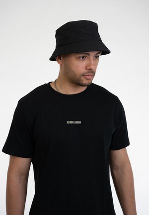 Sort bucket hat lavet af stof med en diskret logo-detalje. Bæres med en enkel sort t-shirt med små hvide tekster. Glat tekstur.