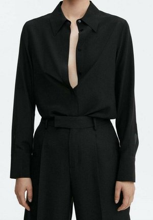 Zwart shirt met lange mouwen en open knopen aan de voorkant, gecombineerd met zwarte hoge taille broek met een brede tailleband.