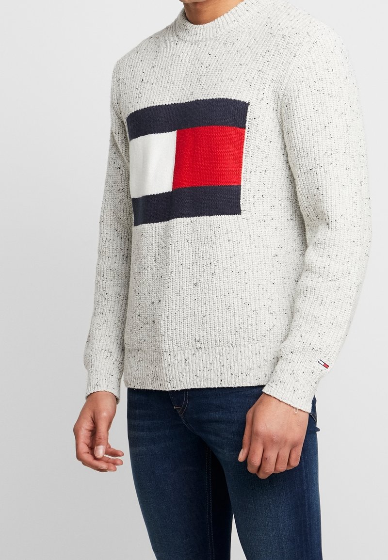 Helle graue Strickjacke mit einem geometrischen Muster in Marineblau, Weiß und Rot auf der Vorderseite; gerippter Kragen und Bündchen; strukturierter Stoff.