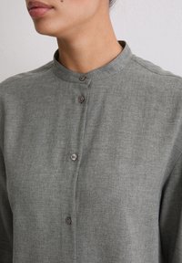 Gray button-up shirt with a mandarin collar, featuring a soft, textured fabric and two buttons visible at the neckline.