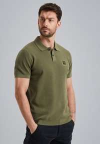Khaki zelená polo košile s texturovanou pletenou látkou, krátkými rukávy a tříknoflíkovou léga. Obsahuje malou nášivku loga na hrudi.