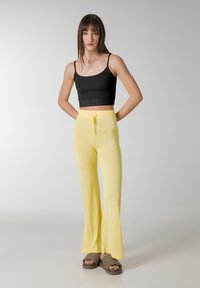 Sort fitted crop top med justerbare stropper, parret med bløde, gule flaired bukser med trækstræk i taljen. Båret med brune slidesandaler.