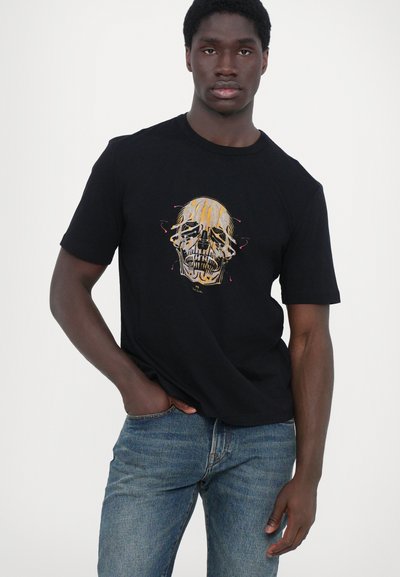 Zwarte t-shirt met korte mouwen met een kleurrijk doodshemd design op de borst. Katoenen stof, relaxte pasvorm, gecombineerd met blauwe jeans.