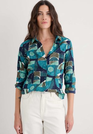 Chemise à col avec boutons en teal et marine, présentant des motifs géométriques abstraits dans des teintes variées avec une texture froissée. Manches longues retroussées.