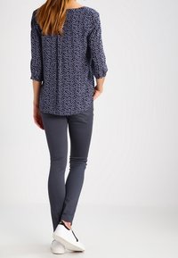 Blouse marine à petit motif floral blanc, manches trois-quarts, associée à un pantalon gris ajusté et des baskets blanches. Texture du tissu lisse.