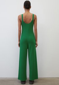 Jumpsuit verde a coste con gambe larghe, schiena a scollo rotondo e spalline spesse. Tessuto testurizzato con una finitura liscia, abbinato a scarpe piattaforma nere chunky.