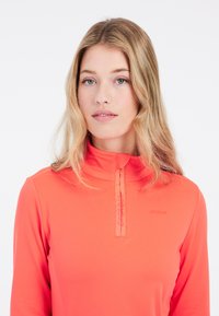 Top corallo a maniche lunghe con colletto a mezza zip. Texture liscia, con un logo discreto sul petto e una vestibilità attillata.