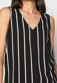 Černý bezramínkový top s V-výstřihem, který má vertikální béžové a bílé pruhy. Lehce svrchní tkanina s uvolněným střihem a centrálním švem.