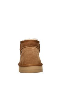 Bruine suède enkellaars met een zachte witte voering, ronde neus en een rubberen zool. Bevat stikseldetails over de bovenkant.