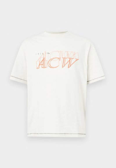 Camiseta de manga corta blanca de algodón. Presenta texto superpuesto y contorneado en color naranja. Dobladillo recto con un sutil detalle de costura.