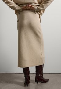 Falda de punto beige con una silueta recta, detalle de dobladillo acanalado, combinada con botas altas de charol burdeos. Textura de tela suave.
