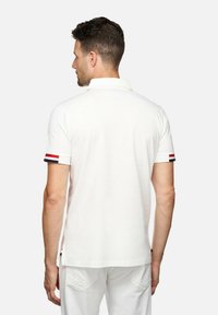 Witte poloshirt met een platte kraag en korte mouwen, voorzien van rode en marineblauwe strepen op de mouwmanchetten. Vloeiende textuur, standaard pasvorm.