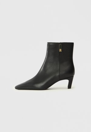 Bota de tornozelo em couro preto com bico pontudo e um pequeno salto. Apresenta um fecho lateral com um detalhe em hardware dourado. Textura suave.