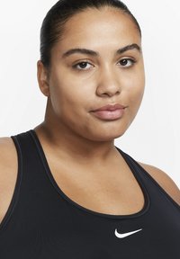 Svart atletisk singlet med rund hals og hvit Nike-logo på brystet. Glatt stoff med en tettsittende design.