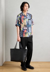 Short-sleeve, multicolored button-up shirt with abstract patterns, black pants, and a large black leather tote bag with dual handles.