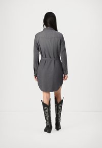 Robe chemise en denim gris avec une taille ceinturée, des manches longues et un ourlet incurvé, associée à des bottes de cowboy noires brodées.